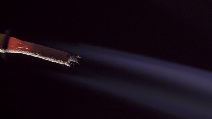 Burning incense stick smoking on simple dark black background, macro copy space, vertical footage