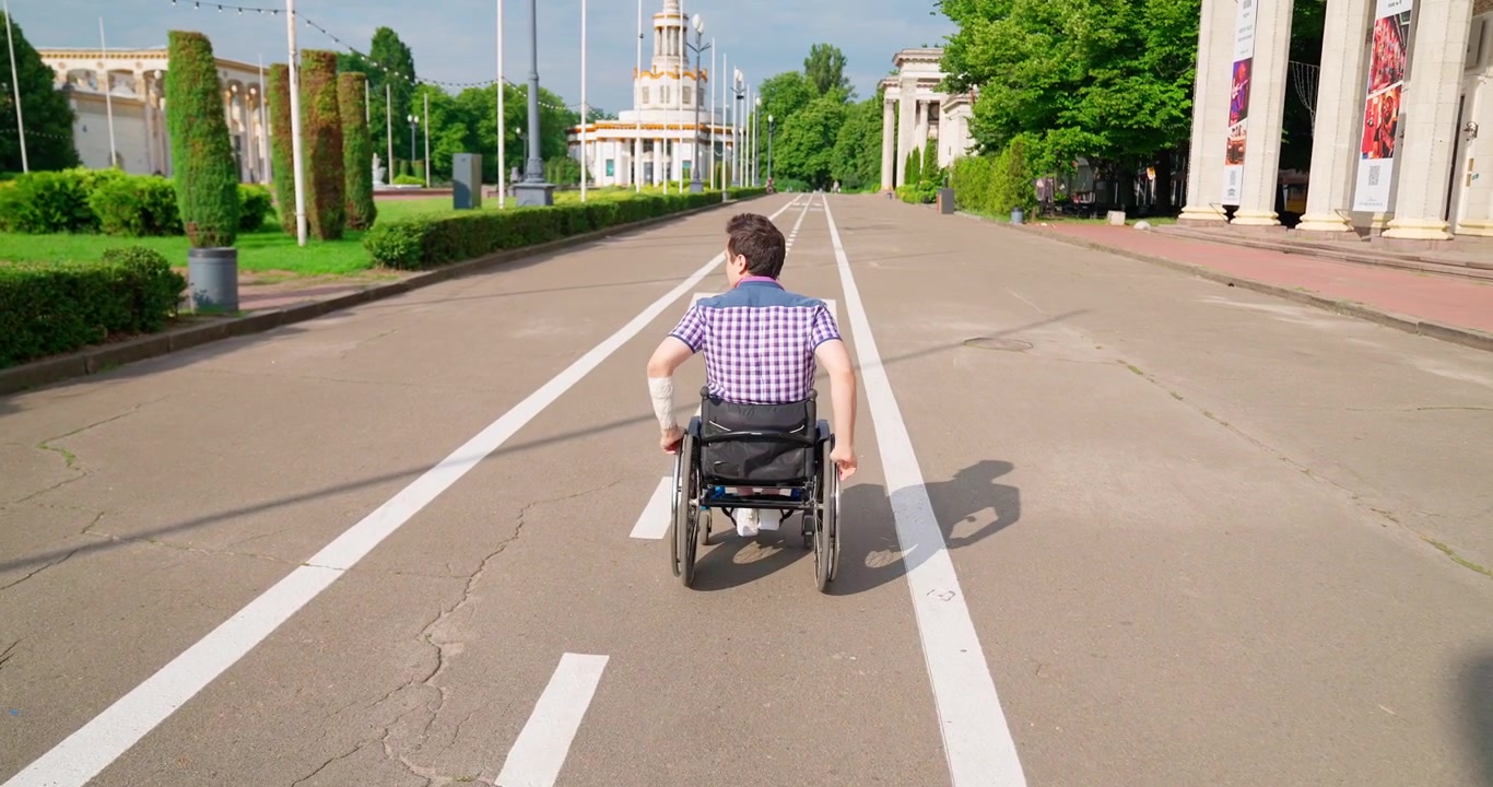 Man in Wheelchair Propelling Himself Forward on a Paved Path in a Park