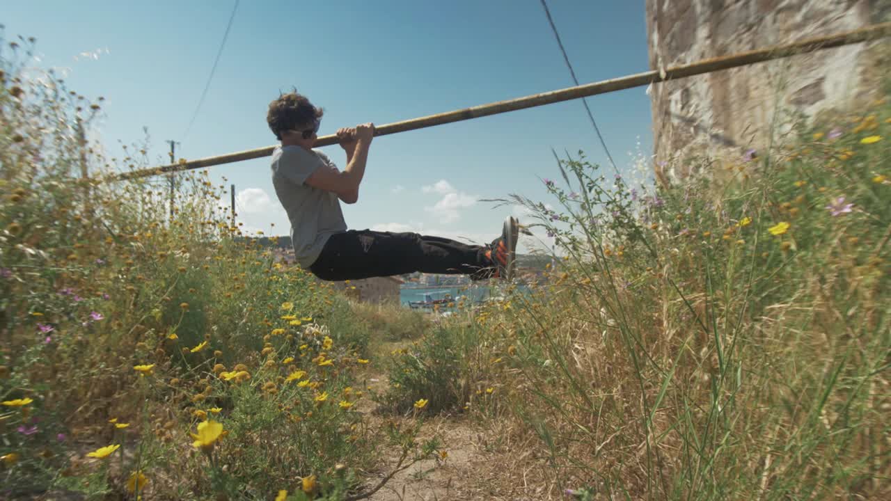 hombre joven en forma hace ejercicio en la calle l-sit pull ups usando un bar al aire libre