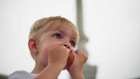 a young child is captured holding a snack near their mouth, seemingly pausing mid-bite while glancing around with curiosity