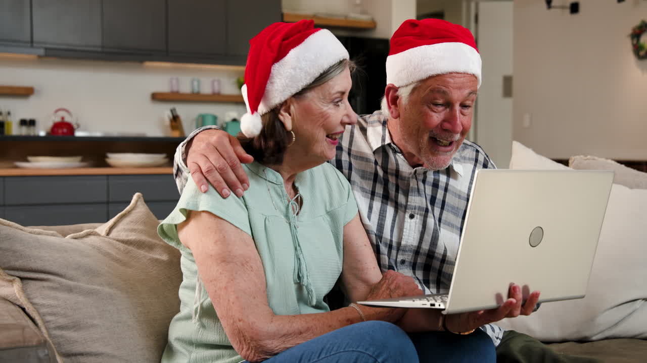 Wearing Santa hats, senior couple video chatting on laptop during Christmas at home