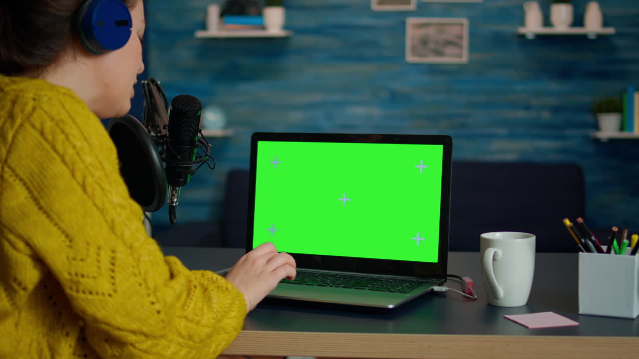 Video blogger reading emails on laptop with green screen display