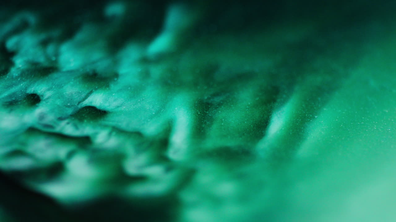 Macro shot of green ink with blue reflections and glitter particles, creating abstract flowing shapes in smooth liquid motion