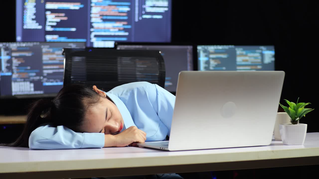 아시아 여성 프로그래머가 에서 코드를 작성하는 동안 잠을 자고 여러 모니터를 사용하여 사무실의 터미널 윈도우 데스크에서 데이터베이스를 표시합니다.