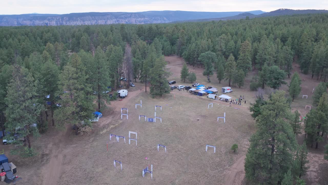 Ilmakuva, jossa drone nousee metsän aukion yläpuolelle paljastaen valaistun kilparadan yöllä. Värikkäät LED-ratavalot näkyvät tummien mäntyjen joukossa. Elokuvamainen nousu esittelee yöllistä moottoriurheilua.