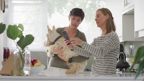 caucasian lesbian couple holding their dog using smartphone at home