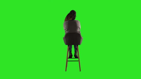 Vista-Trasera,-Fotografía-De-Estudio-De-Una-Mujer-Sentada-En-Un-Taburete-De-Espaldas-A-La-Cámara-Contra-Una-Pantalla-Verde