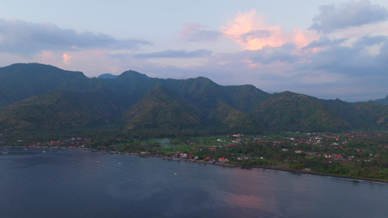 Aerial wide shot of calm coastal waters and mountains under warm evening light