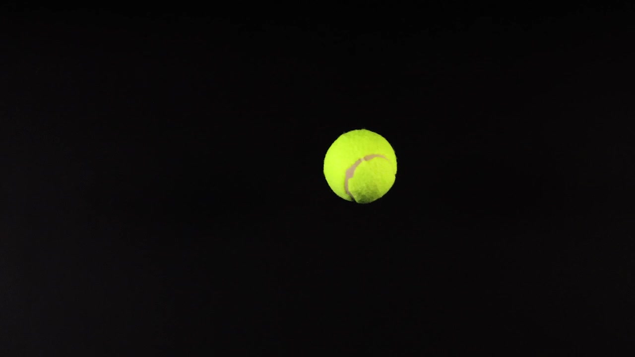 A tennis ball moves across a dark background