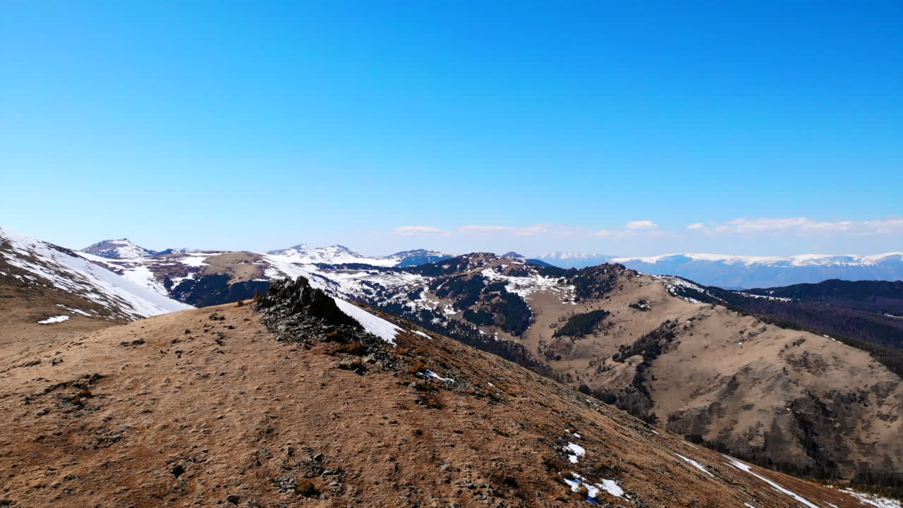 Panorama bjerglandskab med sne og tørt græs under klar blå himmel