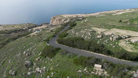 distant view of a car driving fast on the uphill road track overlooking the big blue sea - aerial shot