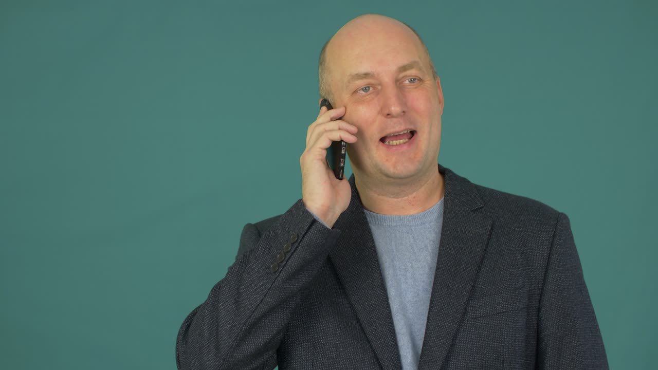 Uomo d'affari calvo di mezza età che sorride e parla allo smartphone.