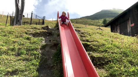 cute young little girl sliding down a slide in slow motion with mountains in the background