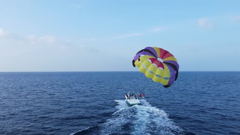 motorboat launching parasailing couple into the sky over blue ocean, drone back view