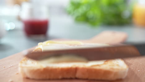esparciendo mantequilla sobre pan ligeramente tostado con un cuchillo de mesa en una tabla de cortar, desayuno en cámara lenta