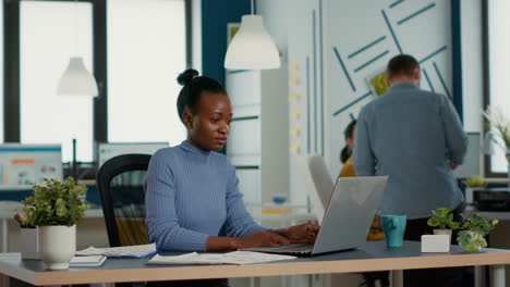 portrait of smiling african american woman working on profit margin and sale statistics using laptop sitting at desk