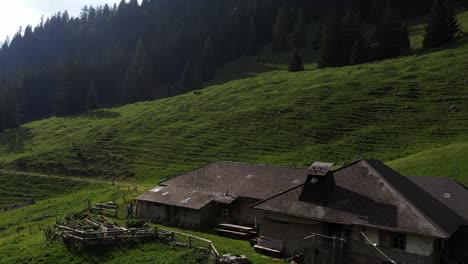 Aerial,-male-backpacker-walking-towards-rural-cabin-by-the-mountains-during-summer