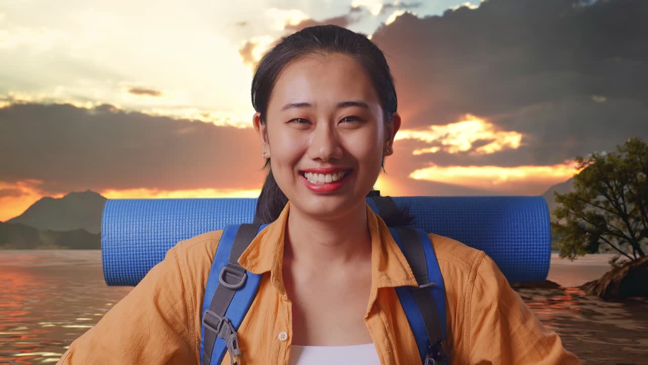 Close Up Of Asian Female Hiker With Mountaineering Backpack Smiling And Posing Arms Akimbo While Standing At A Lake During Sunset Time