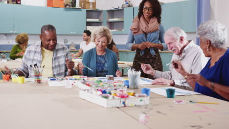 grupo de ancianos jubilados que asisten a clases de arte en un centro comunitario con un maestro