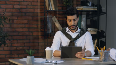 good looking arabian businessman sitting at the desk and working on the tablet, then drinks coffee