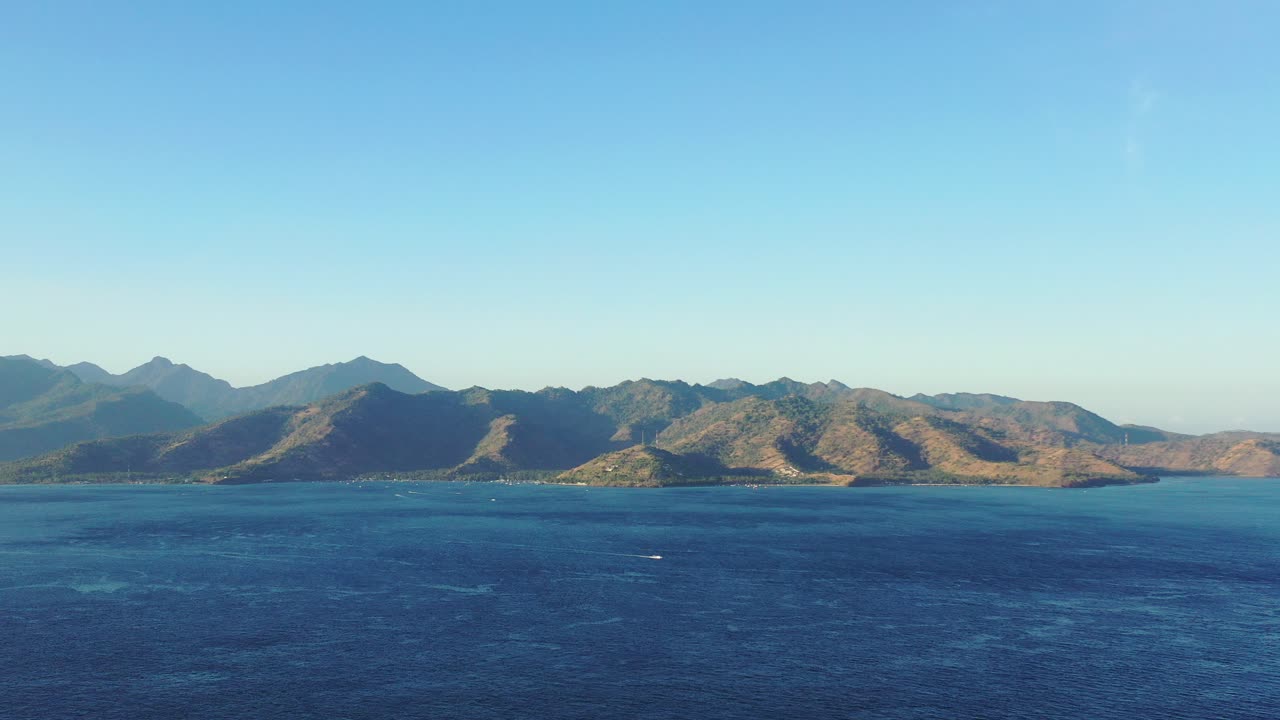 Volcanic mountains of Lombok, Indonesian islands under warm light of sunset, surrounded by deep blue sea on a bright sky background