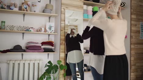 two woman friends fitting knitted cap front mirror in show room