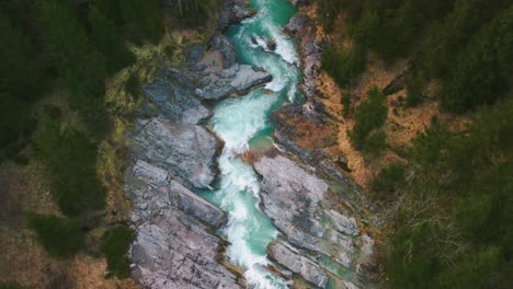 aerial flight above a scenic and idyllic mountain river waterfall canyon with fresh blue water in the bavarian austrian alps, flowing down a beautiful riverbed along trees, forest and rocks from above