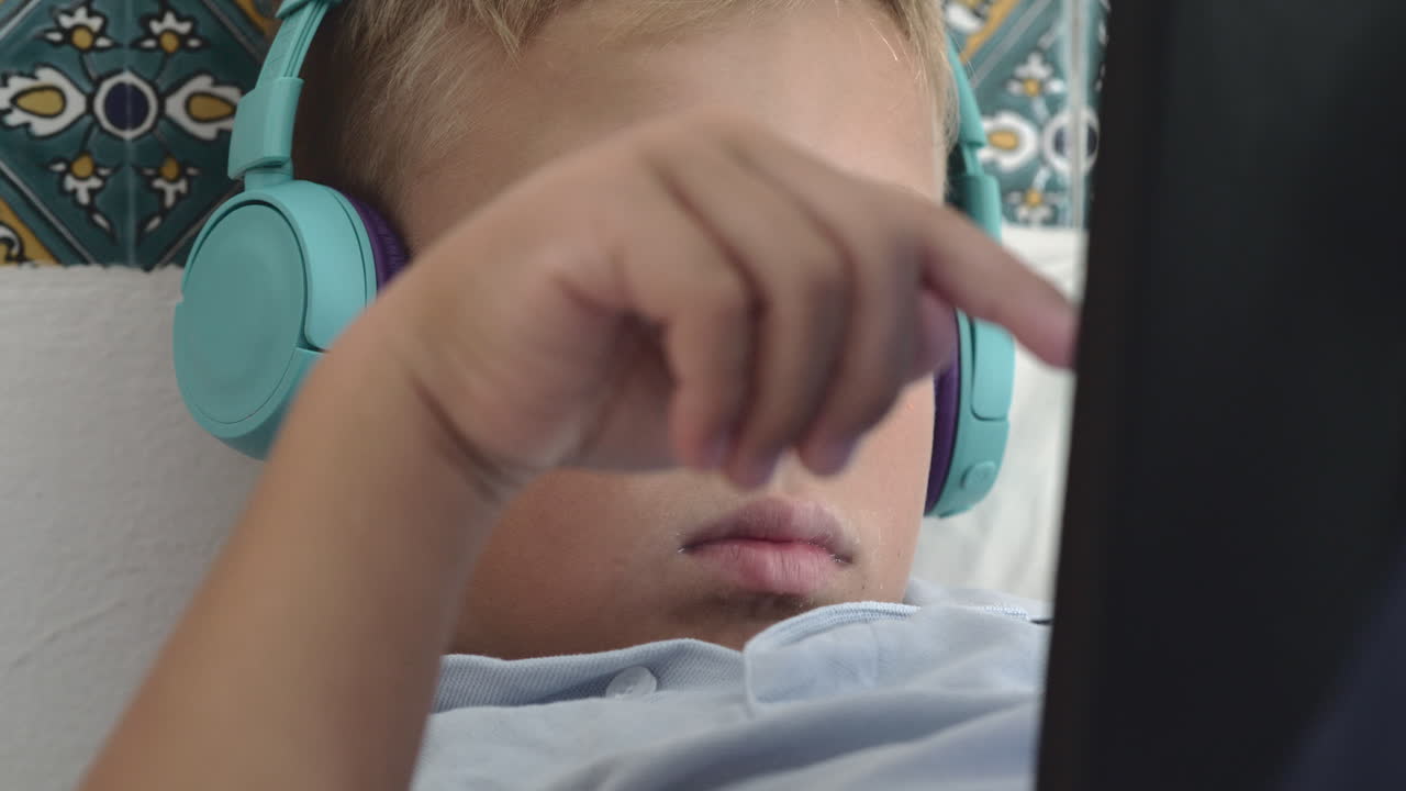 Bored kid in headphones watching something on touch pad