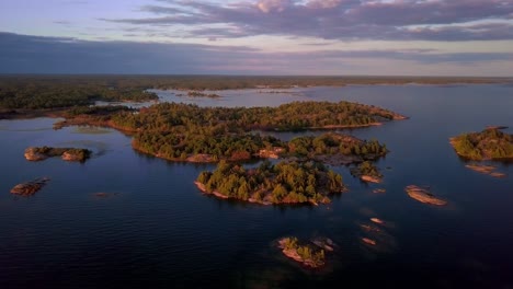 small rocky islands with green pine trees in clear blue lake at sunset, drone aerial wide orbit