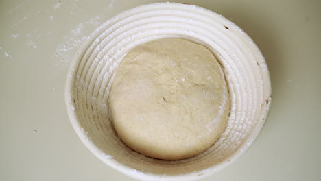 top view of a baker placing the dough into a round banneton proofing basket