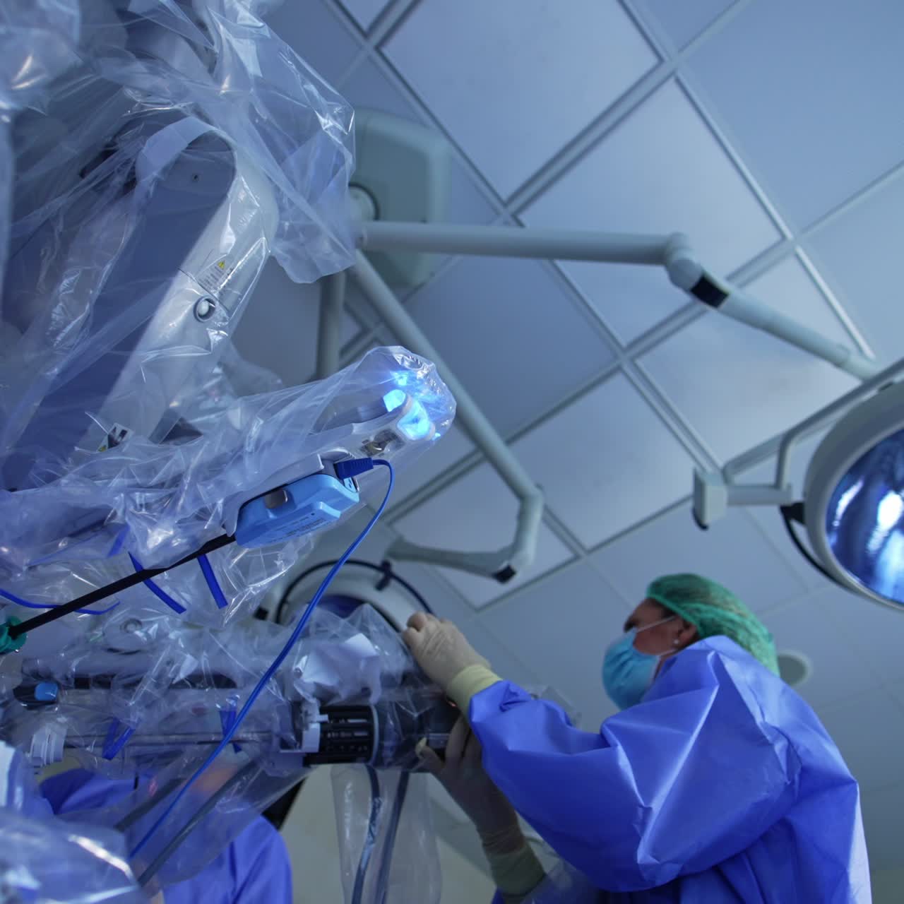 Doctor is pushing and pulling the robotic arms of futuristic equipment covered in plastic. Human and machine interacting at surgical operation. Low angle view
