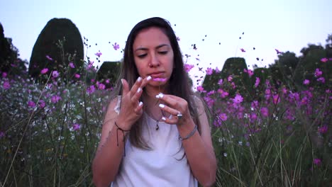 joven latina disfrutando de la naturaleza y oliendo una flor en medio de un hermoso campo morado con flores de hojalata