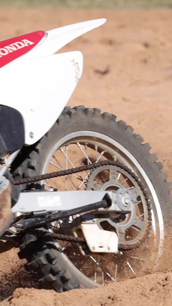 Uma motocicleta acelera por terreno arenoso, levantando terra do pneu traseiro girando.
