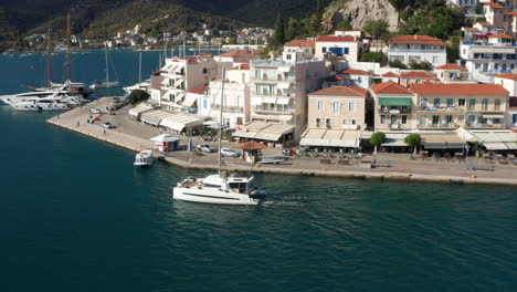 catamaran boat sailing by the terminal with waterfront houses in poros island, greece