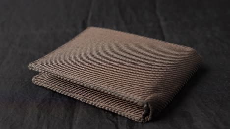 hand laying placing brown fabric wallet on black cloth, close up