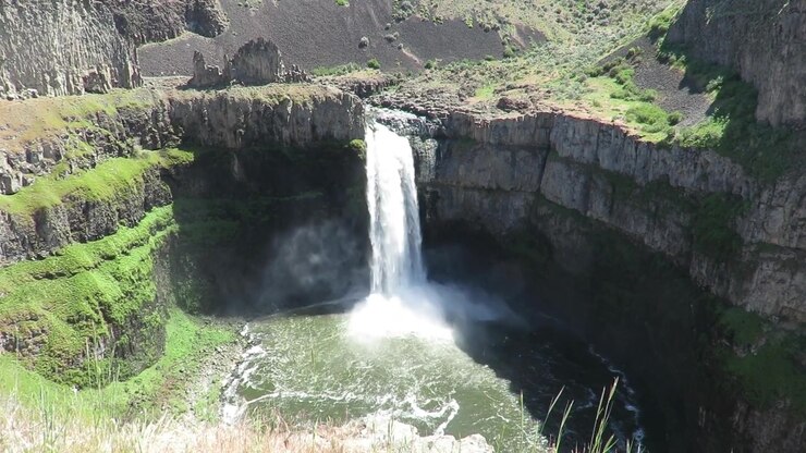 Vista aerea con drone delle cascate Palouse che si gettano da una scogliera di basalto frastagliata in una profonda pozza del canyon. La vegetazione verde copre sezioni del terreno roccioso intorno alla cascata