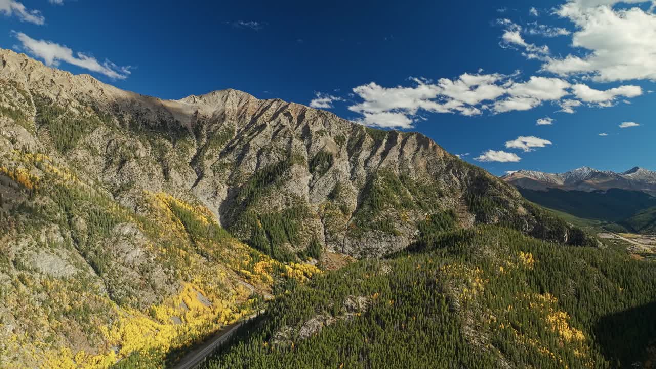 Establishing aerial panoramic pullback over autumn forest valley and mountain road in Frisco Gulch Colorado, vibrant seasonal backdrop