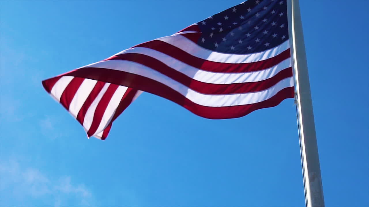 American flag blowing in slow motion against blue sky.