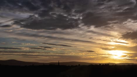 Tag-Nacht-Zeitraffer-Von-Stratocumulus-Wolken,-Die-Durch-Den-Himmel-Rollen,-Während-Die-Sonne-Mit-Bergen-In-Der-Ferne-über-Dem-Horizont-Untergeht