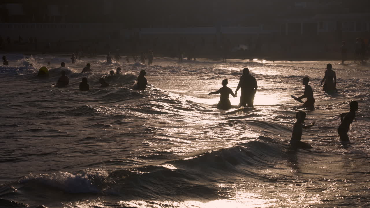 People enjoying the waves at the beach at sunset