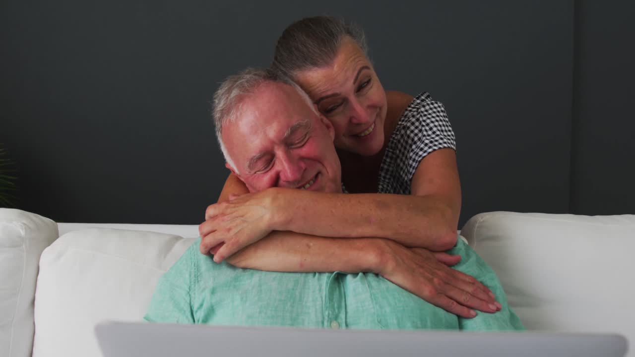 Happy caucasian senior couple embracing on sofa and talking