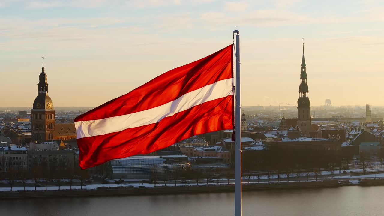 Latvian flag glows in golden sunrise over snowy Old Riga, winter morning scene