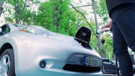 refueling process of an electric car. a shot under the hatch where the electric eco car charges. the electric car charging hatch opens automatically. a male hand inserts an erectile car