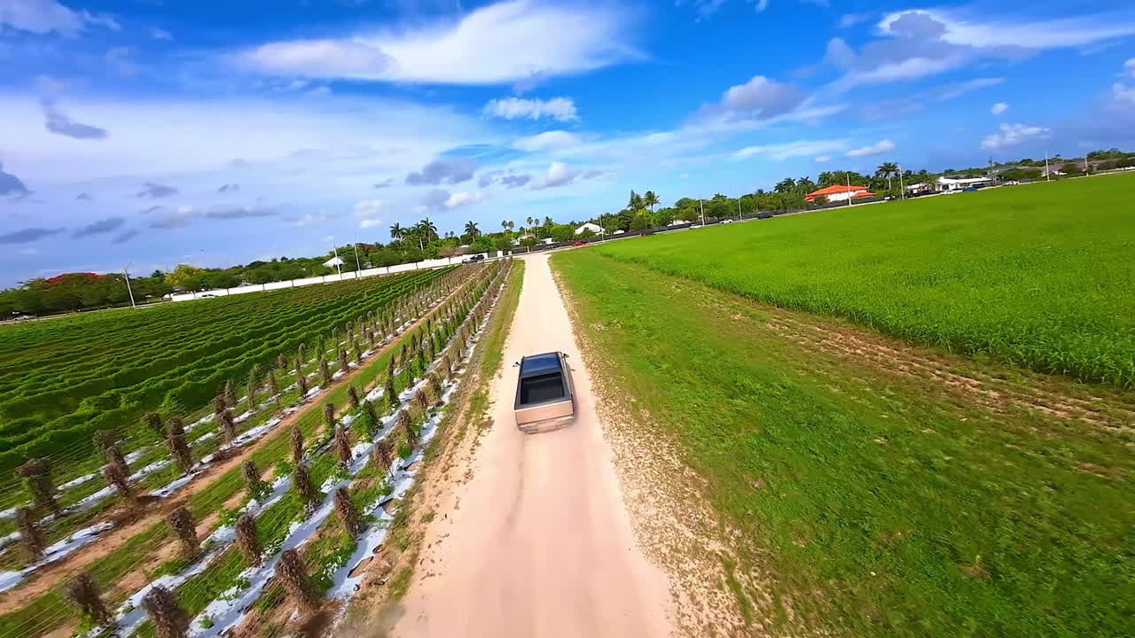 Tesla Cybertruck approaches the road where other cars ride. Testing electric car in the rural area. FPV drone footage.