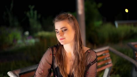 Hermosa-Joven-Con-Maquillaje-De-Noche-Sentada-En-Un-Banco-En-Un-Parque-Iluminado-Por-La-Noche