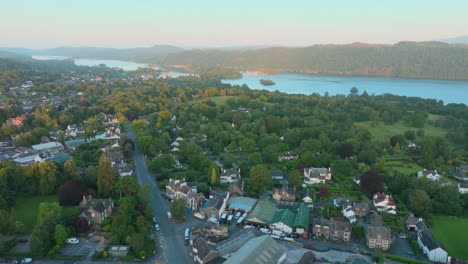 flying over lakeside rural town towards large lake at sunrise. summer. windermere, cumbria, uk