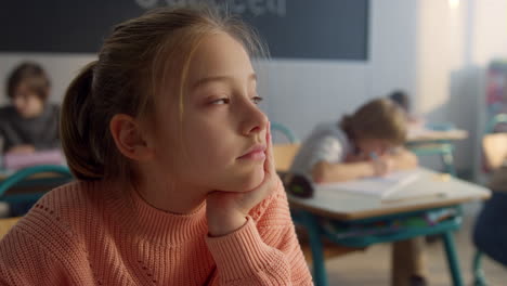 dreamy kid sitting at desk in classroom. thoughtful schoolgirl looking at window