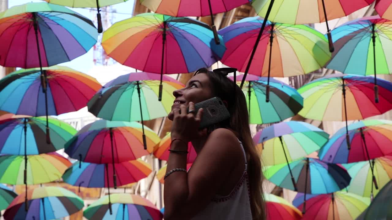 Ragazza che parla al telefono sorridendo in una strada con ombrelli colorati