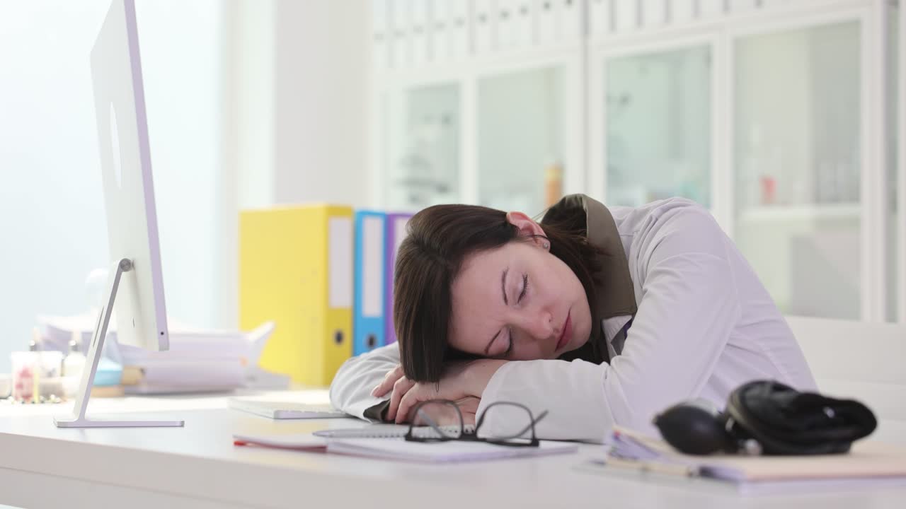 Donna stanca dorme sulla scrivania dell'ufficio vicino agli occhiali dopo gli straordinari.
