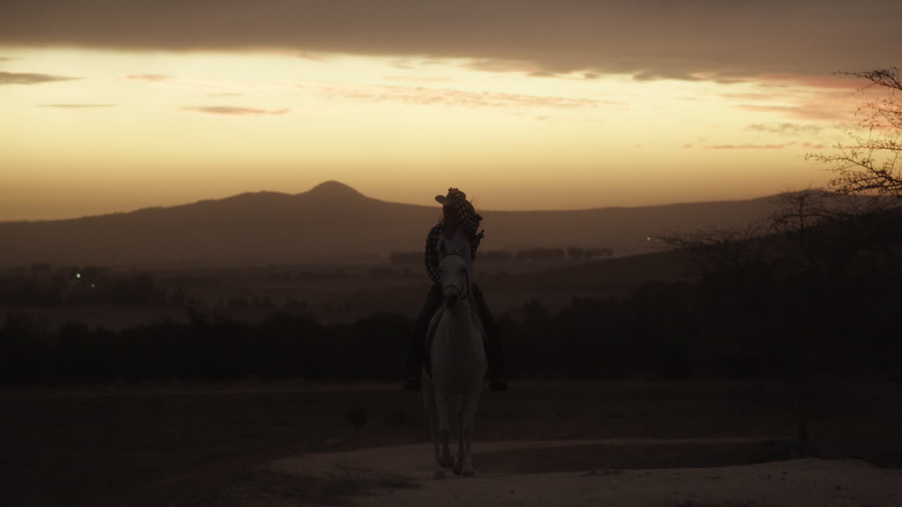 una mujer joven montando un caballo en un rancho al atardecer